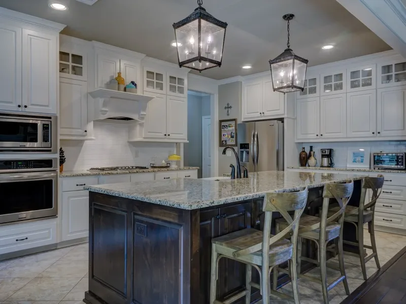 A picture of a kicthen with lighting & cabinets in a white and black theme with granite